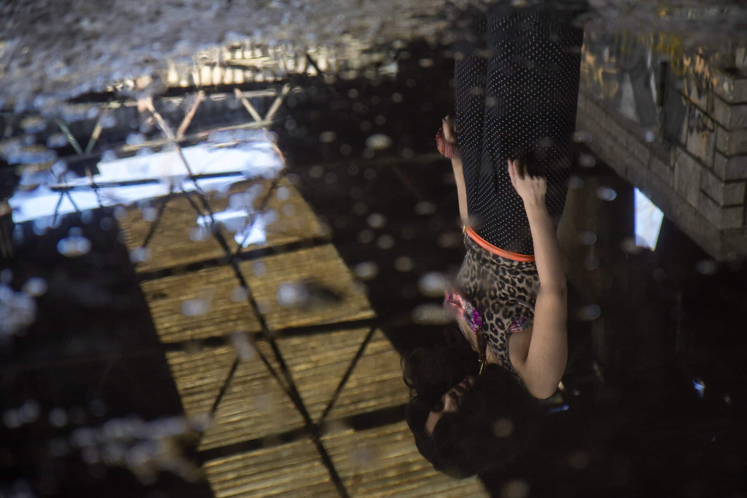 Die Spiegelung einer Frau in einer Pfütze. Sie hält eine Kamera in der Hand und fängt die Szene ein. Die Details einer Brücke und eines Himmels, die sich im Wasser spiegeln, sind klar zu erkennen. © Fotografie Tomas Rodriguez